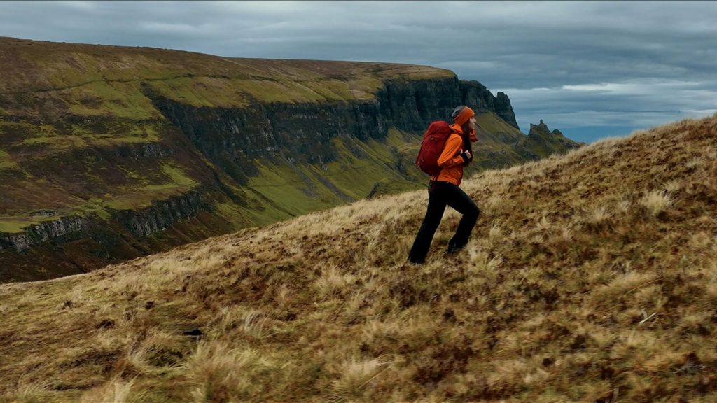 A woman in a raincoat hikes up the Isle of Skye in Scotland
