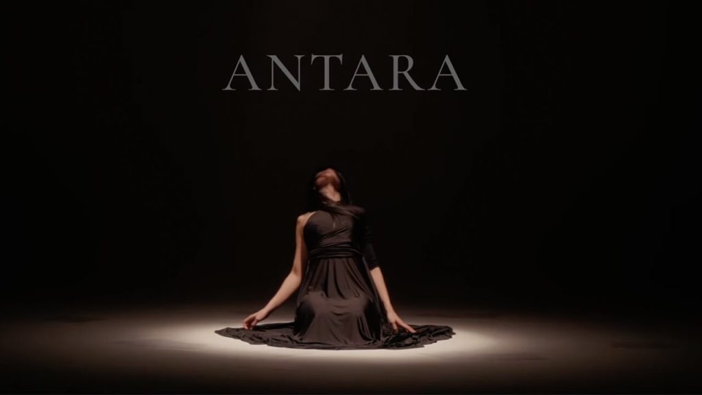 Antara. A woman kneeling on the floor is looking up into the darkness, we can't see her face